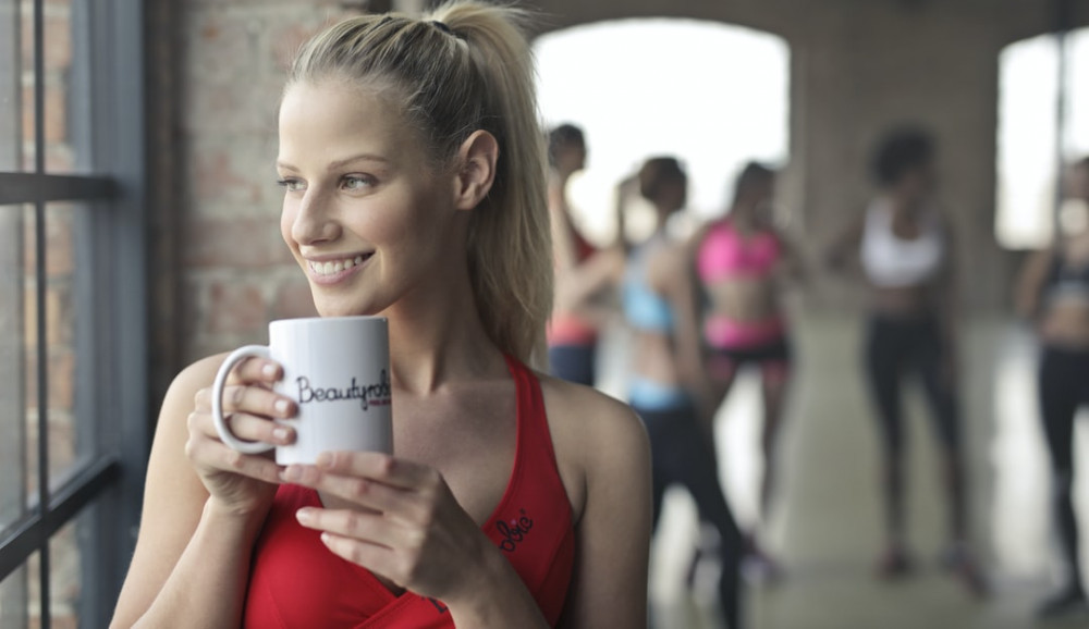 Young blonde woman at the gym drinking from a coffee mug